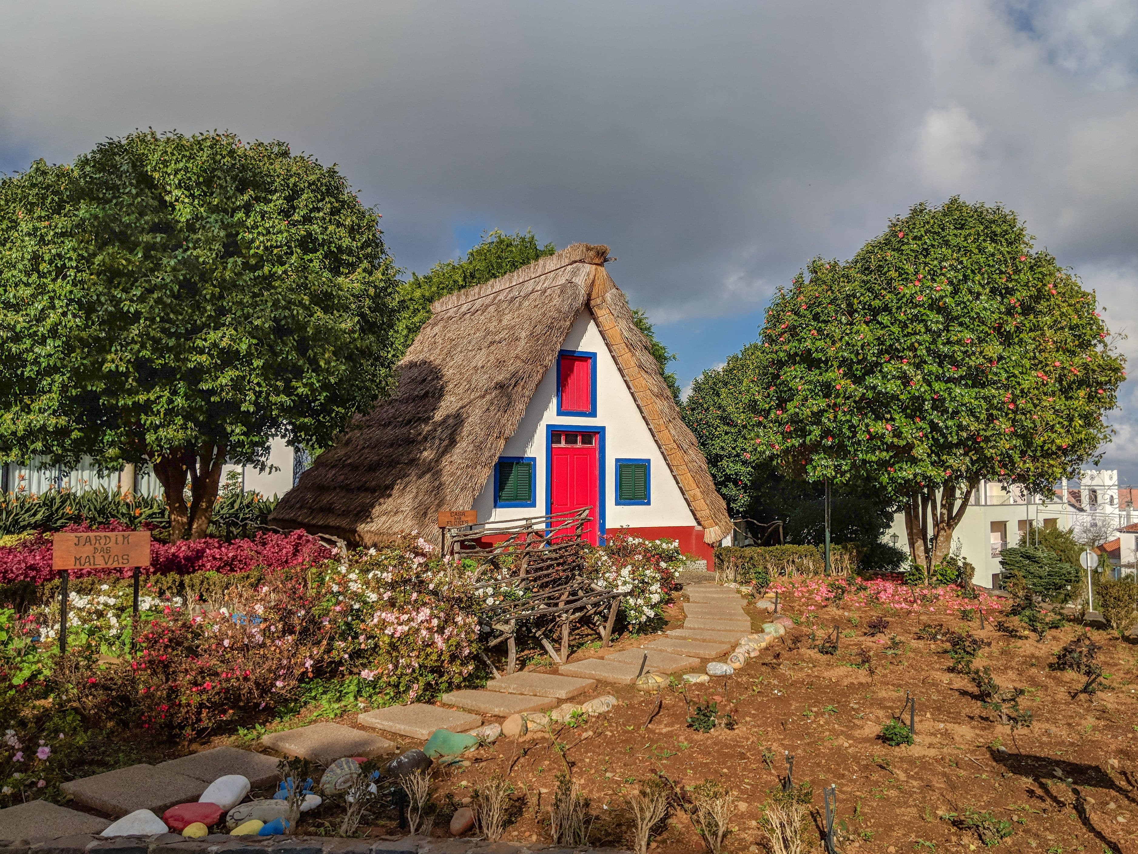 A traditional thatched A-frame house in Santana, painted white, red and blue and set among flower gardens.
