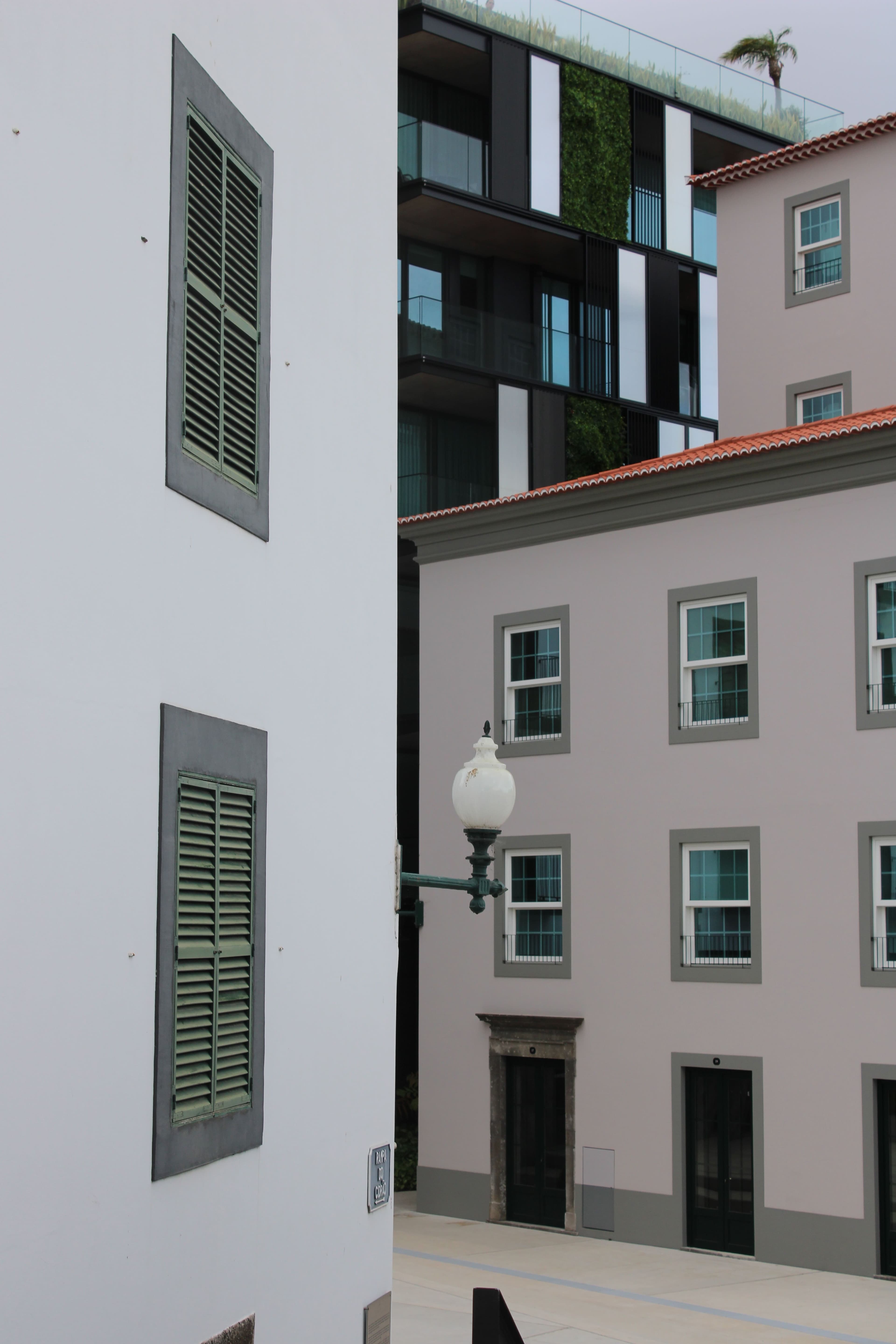 A modern apartment block beside a traditional white building with green shutters in Funchal.